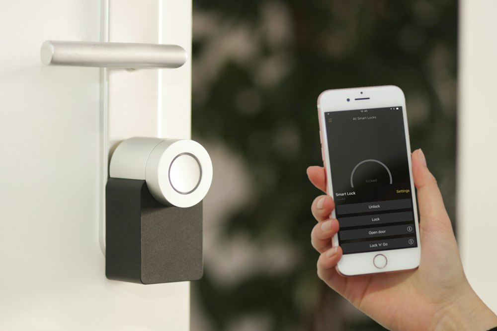 A hand holding a phone beside a smart door lock